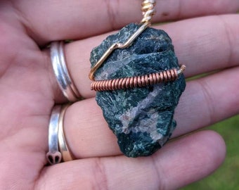 May include: A green stone pendant wrapped in gold and copper wire, hanging from a brown leather cord.