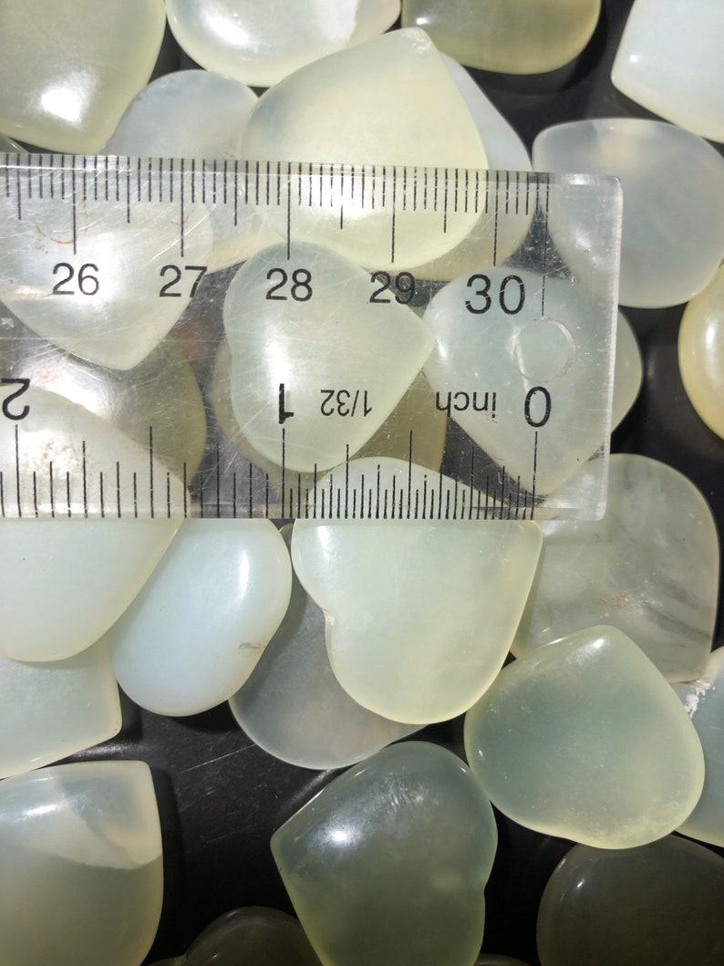 May include: A close-up of a group of white heart-shaped stones, with a ruler measuring one of the stones at approximately 1 inch in length.