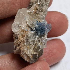 May include: A cluster of clear quartz crystals with a blue crystal in the center. The crystals are clustered together in a rough, natural formation.