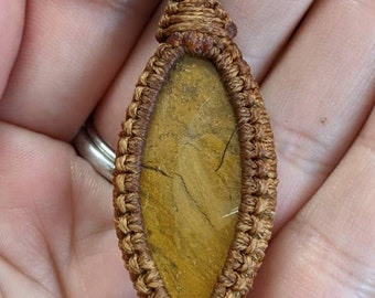 May include: A brown leather cord necklace with a knotted pendant featuring a brown and gold oval stone.