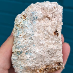 Puede incluir: Una roca rugosa, blanca y gris con cristales azul verdosos. La roca tiene una superficie rugosa y texturizada.