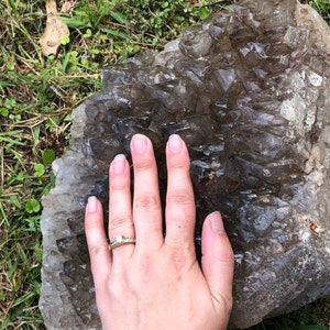 May include: A large, flat, gray rock with a layer of clear quartz crystals on top. The crystals are arranged in a pattern of overlapping, pointed shapes.