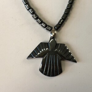 May include: A black hematite necklace with a black hematite pendant shaped like a bird with wings spread out.