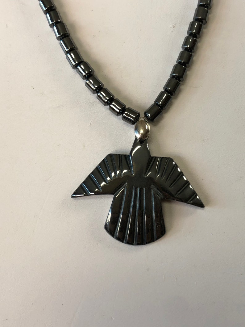 May include: A black hematite necklace with a black hematite pendant shaped like a bird with wings spread out.
