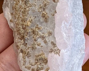 May include: A clear quartz crystal with a pink and white layer and brown inclusions. The crystal has a rough, natural texture.