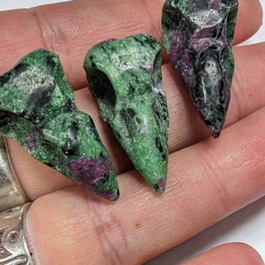 Op de afbeelding: Drie groene en paarse edelsteen vogel schedel sculpturen. De schedels zijn gesneden uit een groene en paarse steen met een gevlekt patroon.