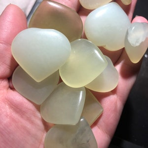 May include: A collection of ten heart-shaped, pale green jade stones. The stones are smooth and polished, with a slight translucence.