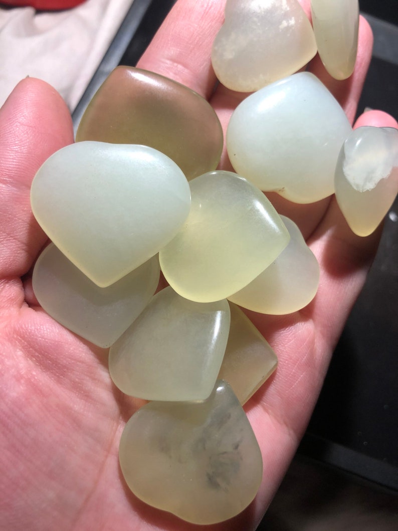 May include: A collection of ten heart-shaped, pale green jade stones. The stones are smooth and polished, with a slight translucence.