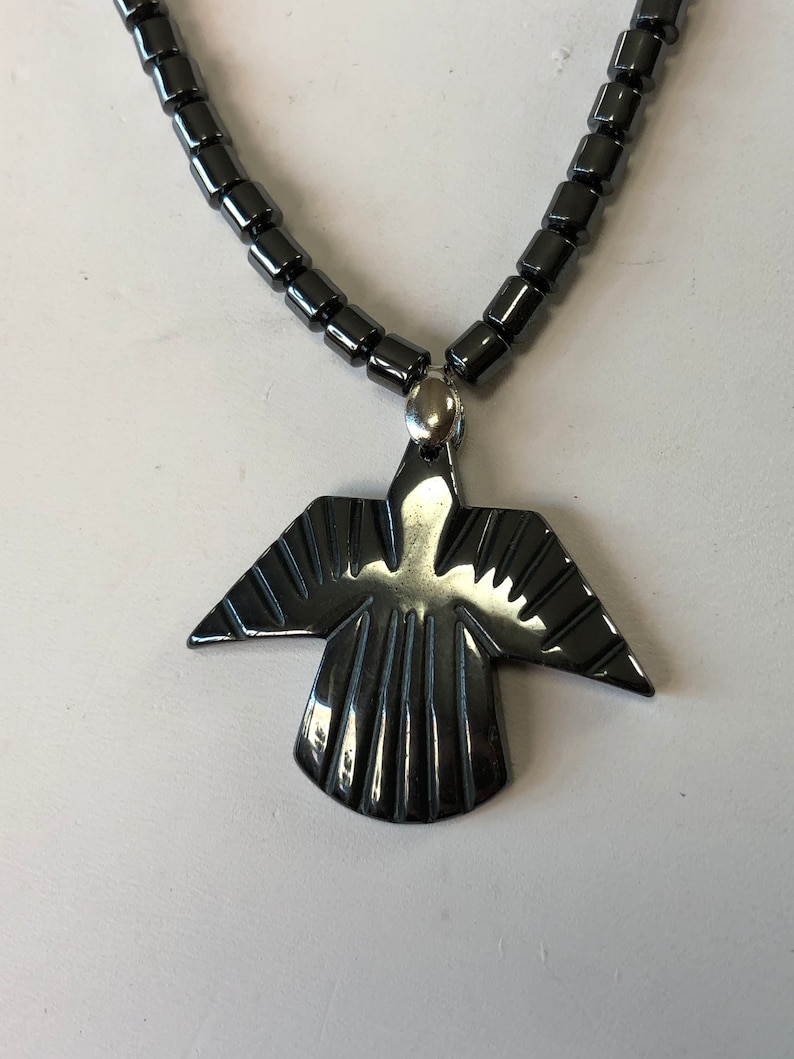 May include: A black hematite necklace with a carved hematite bird pendant. The necklace is made of small, round beads.