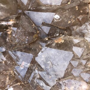 May include: Close-up of a cluster of clear quartz crystals with a smoky brown hue. The crystals are faceted and have a natural, rough texture.