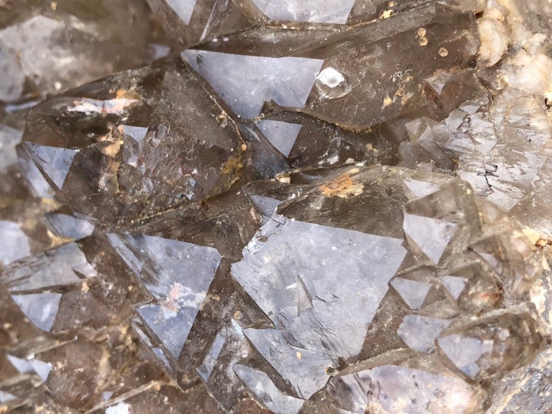 May include: Close-up of a cluster of clear quartz crystals with a smoky brown hue. The crystals are faceted and have a natural, rough texture.