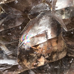 May include: A cluster of smoky quartz crystals with a rainbow iridescence. The crystals are clear and have a rough, natural texture.