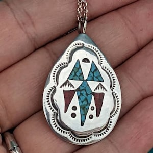 May include: A silver teardrop-shaped pendant with a turquoise and red geometric design. The pendant is on a silver chain.
