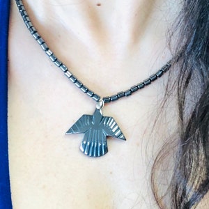 May include: A black necklace with a black bird pendant. The necklace is made of small, round beads.