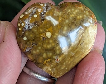 May include: A heart-shaped polished stone with a brown and yellow color and white and yellow spots.