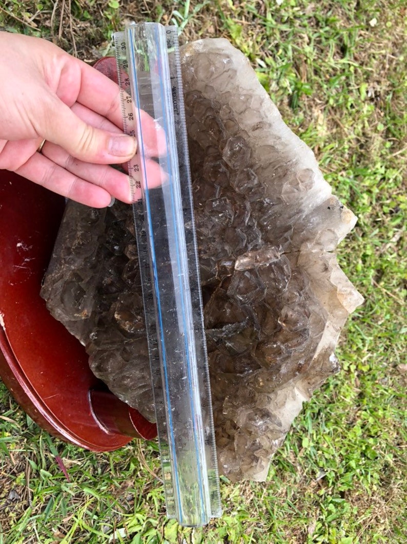 May include: A large, clear quartz crystal cluster with a ruler for scale. The crystal is approximately 30 inches long and has a brown, smoky hue.