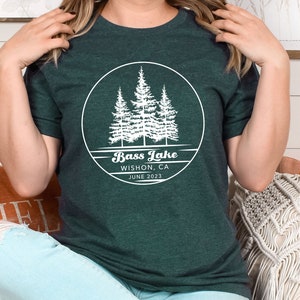 May include: A dark green t-shirt with a white circle graphic featuring three pine trees and the text "Bass Lake, Wishon, CA, June 2023".