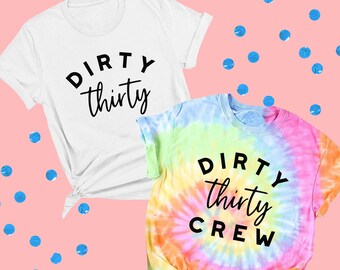 May include: Two t-shirts with the text "Dirty Thirty" and "Dirty Thirty Crew" printed on them. The first shirt is white and the second shirt is a tie-dye pattern with rainbow colors.