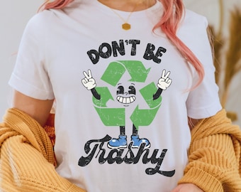 May include: White t-shirt with a green recycling symbol with a face and arms. The symbol is holding up peace signs. The text "Don't Be Trashy" is printed below the symbol.