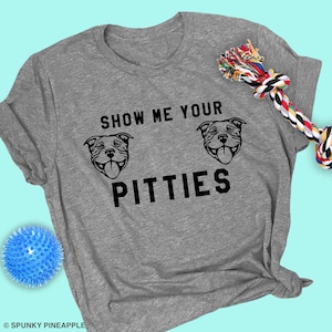 May include: Gray t-shirt with the text "Show me your Pitties" and two black and white pit bull dog illustrations.