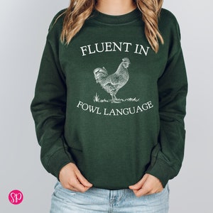 May include: A dark green sweatshirt with a white rooster illustration and the text "Fluent in Fowl Language".
