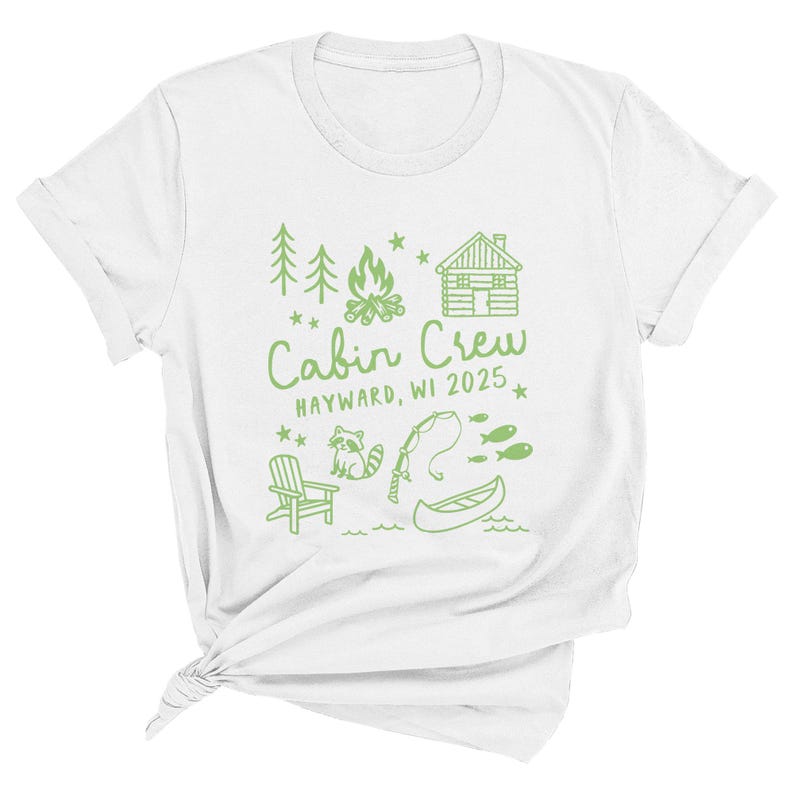 K&ouml;nnte beinhalten: Wei&szlig;es T-Shirt mit einem gr&uuml;nen Grafikdesign. Das Design enth&auml;lt den Text "Cabin Crew HAYWARD, WI 2025" sowie Illustrationen einer H&uuml;tte, B&auml;ume, ein Lagerfeuer, ein Waschb&auml;r, eine Angelrute, Fische, ein Kanu und einen Stuhl.