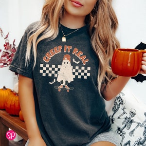 May include: A black t-shirt with a graphic of a ghost skateboarding and the text "Creep It Real" in a retro font.