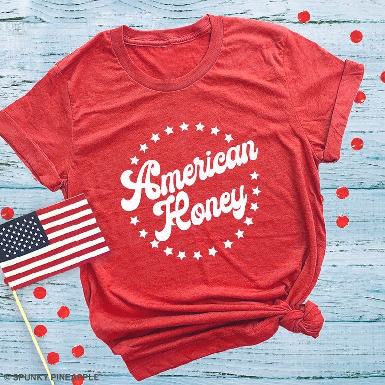 K&ouml;nnte beinhalten: Rotes T-Shirt mit einem wei&szlig;en Kreisdesign, auf dem in einer Retro-Schrift "American Honey" steht. Der Kreis ist von wei&szlig;en Sternen umgeben.
