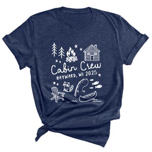 May include: Navy blue t-shirt with a white graphic design. The design includes a cabin, campfire, trees, raccoon, fishing rod, canoe, and the text "Cabin Crew 2025, Hayward, WI". A casual tee for outdoor enthusiasts.