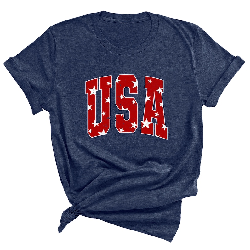 K&ouml;nnte beinhalten: Ein marineblaues T-Shirt mit einer roten "USA"-Grafik. Die Buchstaben sind mit wei&szlig;en Sternen gef&uuml;llt.