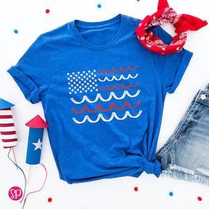 May include: A blue t-shirt with a white and red American flag design. The flag is made up of wavy lines instead of stripes.