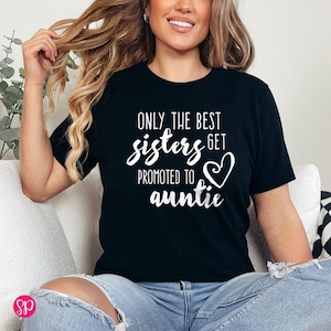 May include: Black t-shirt with white text that reads "ONLY THE BEST sisters GET PROMOTED TO auntie" with a heart graphic. The shirt is a crew neck and is being worn by a person.