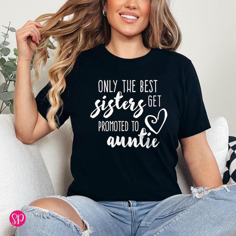 May include: Black t-shirt with white text that reads "ONLY THE BEST sisters GET PROMOTED TO auntie" with a heart graphic. The shirt is a crew neck and is being worn by a person.