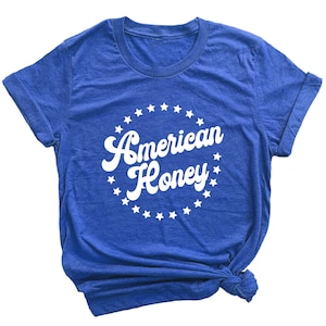 K&ouml;nnte beinhalten: Ein k&ouml;nigsblaues T-Shirt mit einem wei&szlig;en Kreisdesign, das den Text "American Honey" in einer Retro-Schriftart zeigt, umgeben von wei&szlig;en Sternen.