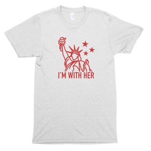 Puede incluir: Una camiseta gris jaspeada con un contorno rojo de la Estatua de la Libertad y el texto "I'M WITH HER".