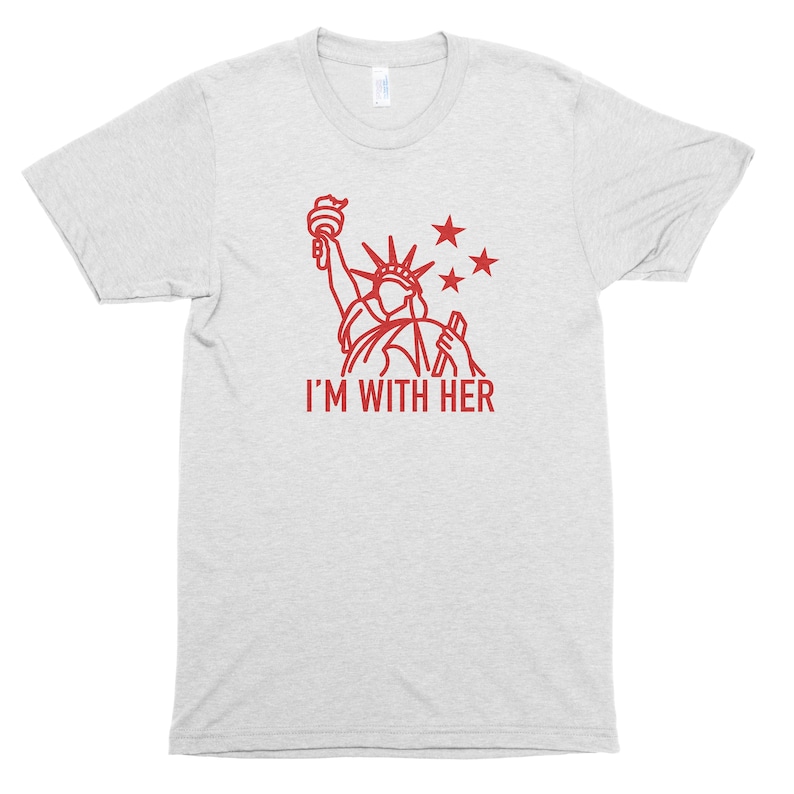 Puede incluir: Una camiseta gris jaspeada con un contorno rojo de la Estatua de la Libertad y el texto "I'M WITH HER".