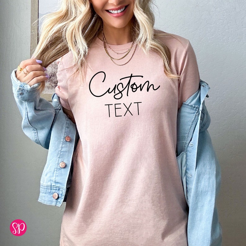 May include: A light pink t-shirt with the text "Custom Text" in black script font.