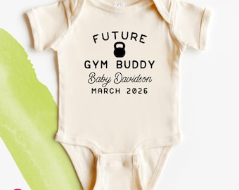 May include: A cream-colored short-sleeve baby bodysuit featuring black text that reads FUTURE GYM BUDDY, Baby Davidson, and MARCH 2026, with a black kettlebell icon positioned between the words FUTURE and GYM BUDDY.