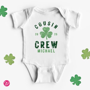 May include: White baby bodysuit with green shamrock graphic and the text "COUSIN CREW MICHAEL 20 25".