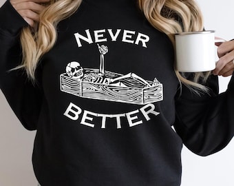 May include: A black crewneck sweatshirt featuring a white graphic of a skeleton lying in a wooden coffin with one arm raised in a thumbs-up gesture. The text NEVER is printed above the coffin and BETTER is printed below in white letters.