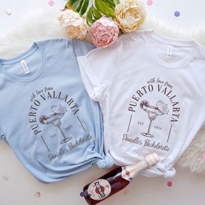May include: Two light blue and white t-shirts with a margarita graphic and the text "with love from Puerto Vallarta Est. 2024 Danielle's Bachelorette" printed on them.