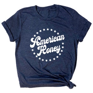 K&ouml;nnte beinhalten: Ein marineblaues T-Shirt mit einem wei&szlig;en Kreisdesign mit dem Text "American Honey" umgeben von wei&szlig;en Sternen.