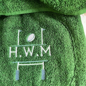 May include: Green towel with embroidered rugby goal posts and a rugby ball. The text "H.W.M." is embroidered below the goal posts.