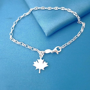 Peut inclure: Un bracelet en chaîne argentée doté d'un pendentif en forme de feuille d'érable polie. Le bracelet est composé de maillons ovales interconnectés et comprend un fermoir mousqueton sécurisé pour attacher le bijou autour du poignet.