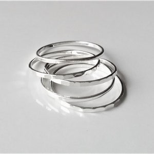 May include: Five silver hammered stacking rings. The rings are thin and delicate, and they are stacked on top of each other.