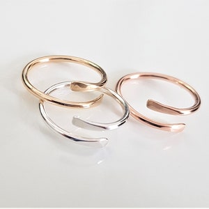May include: Three simple open rings in gold, silver, and rose gold. The rings are made of a single piece of metal that is bent into a circle and then twisted to create a unique design.