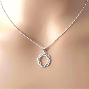 May include: A silver-toned necklace featuring a delicate chain and a circular pendant. The pendant is composed of a continuous, twisted metal design that forms an open, ring-like shape. The metal has a polished, reflective finish throughout.