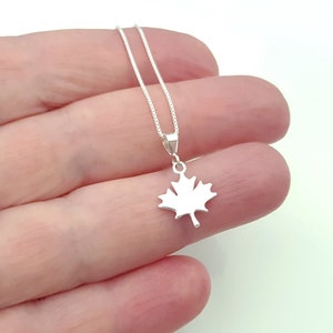 May include: A silver maple leaf pendant necklace. The pendant, a detailed cutout of a maple leaf, hangs from a fine silver chain. The necklace is displayed against a light background.