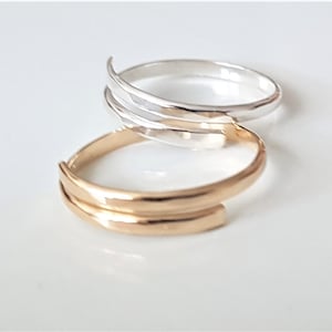 May include: Two simple, minimalist rings, one gold and one silver, stacked on top of each other. Both rings are made of a single band with a slightly curved edge.