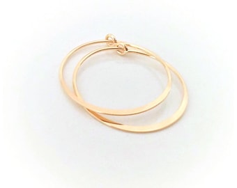May include: A pair of thin, circular hoop earrings crafted from a polished, warm-toned gold metal. The earrings feature a simple, continuous wire design with a small, integrated clasp mechanism at the top where the two ends meet to form a complete circle.